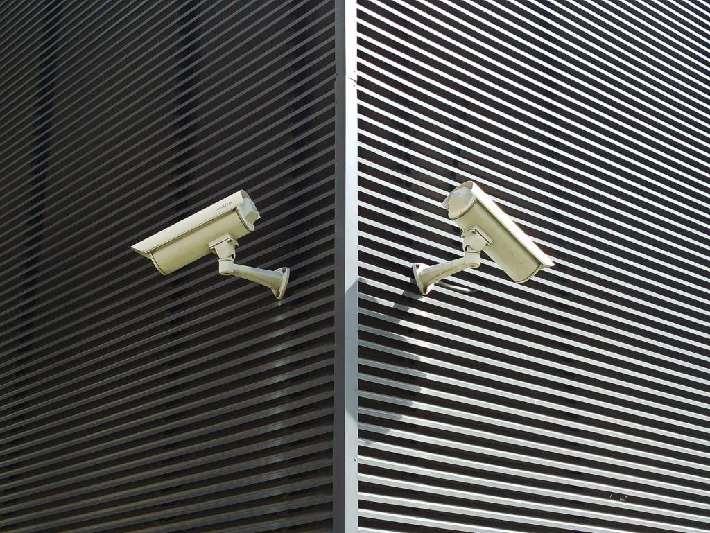 Two security cameras mounted on a slatted wall for surveillance