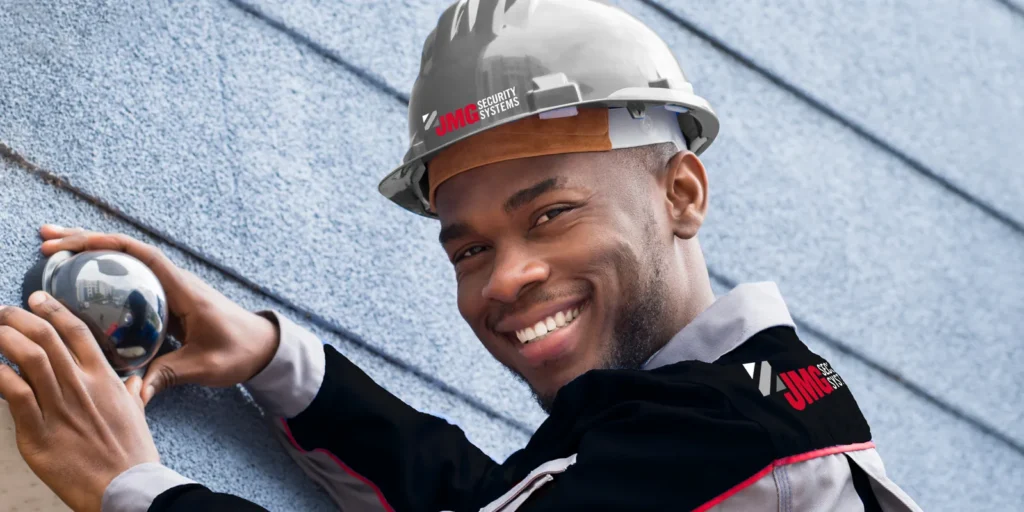 A JMG technician in a hard hat smiling as he fits a dome camera to a wall
