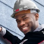 A JMG technician in a hard hat smiling as he fits a dome camera to a wall